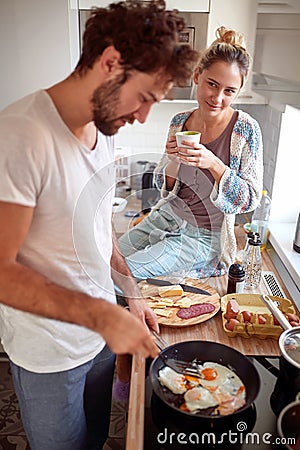 Beardy young man with curly hair making breakfast, while his female partner looking with love at him Stock Photo