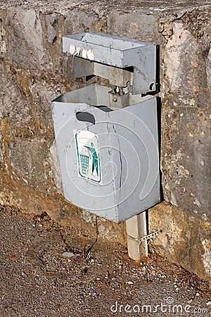 Beaten down grey metal public trash can mounted on stone wall Stock Photo