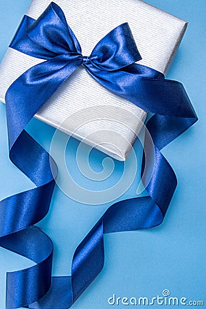 Beatiful silver gift box with blue atlas bow on a pastel blue background. Image for your design Stock Photo