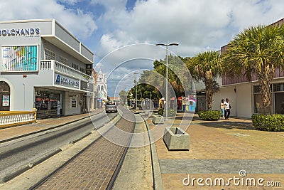 Beatiful view of one of streets of Oranjestad. Buildings and green trees along tram rails on blue sky with white clouds background Editorial Stock Photo