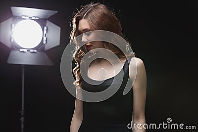 Beautfiul young woman standing near studio spotlight Stock Photo