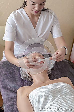 Beautician apply collagen mask to woman face. Cosmetologist works with a woman in a spa salon Stock Photo