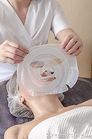 Beautician apply collagen mask to woman face. Cosmetologist works with a woman in a spa salon Stock Photo