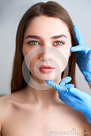 Beautician doctor`s hands in gloves touching face of attractive woman. Fashion blonde model after cosmetic treatment Stock Photo