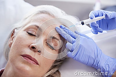 Beautician Giving Mature Female Patient Botox Injection In Forehead Stock Photo