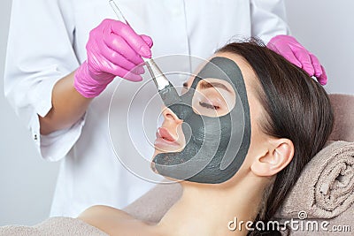 Beautician makes a black clay mask to rejuvenate the skin to beautiful woman.Cosmetology concept and treatment of problem skin Stock Photo