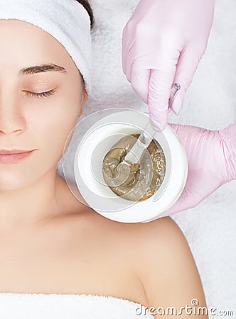 Beautician makes a face clay mask against acne on the face of a woman to rejuvenate the skin. Cosmetology treatment of problem Stock Photo