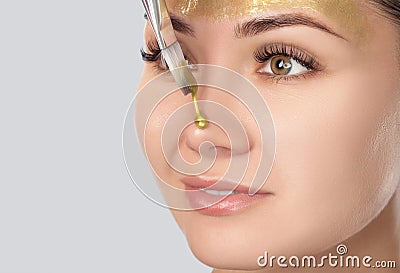 Beautician makes a face mask with gold particles on the face of a woman to rejuvenate the skin. Cosmetology treatment of problem Stock Photo