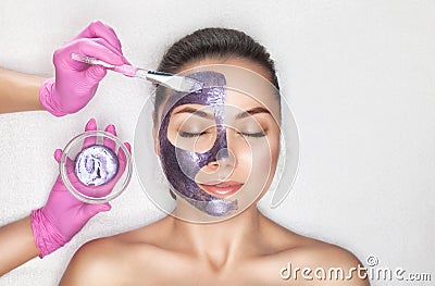 Beautician makes a face mask with purple particles on the face of a woman to rejuvenate the skin. Cosmetology treatment of problem Stock Photo