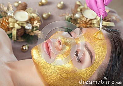 Beautician makes a golden mask to rejuvenate the skin to beautiful woman. Next to her are Christmas decorations.New Year`s and Stock Photo