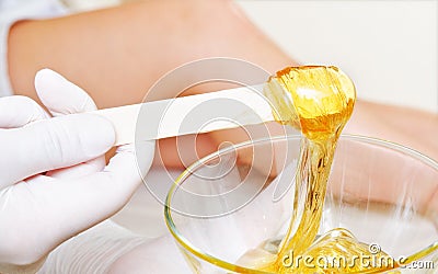 Beautician master holding bowl with hot wax for depilation epilation hair removal procedure and female legs on blurred background Stock Photo