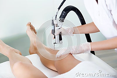 The beautician`s hands removing legs hair with a laser to her client in the beauty salon. Stock Photo