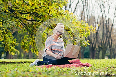 Senior woman resting in the park sitting on the grass, using phone and laptop, and reading a book Stock Photo