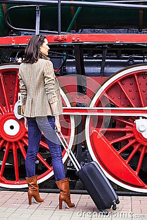 Beautiful adult woman traveler with a suitcase on the platform near the huge wheels Stock Photo