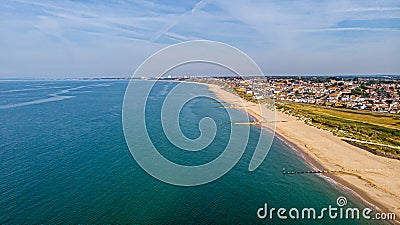 A beautiful aerial seaside view with sandy beach, crystal blue water, groynes breakwaters and green vegetation dunes along a Stock Photo