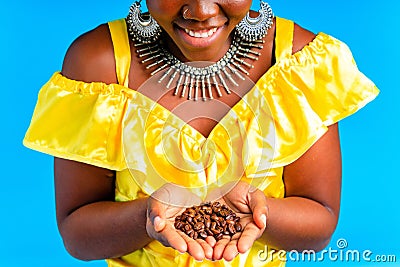 beautiful africa-american woman with yellow turban ower the head showing fresh coffee beand in studio blue baclground Stock Photo