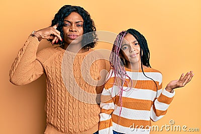 Beautiful african american mother and daughter wearing wool winter sweater confused and annoyed with open palm showing copy space Stock Photo