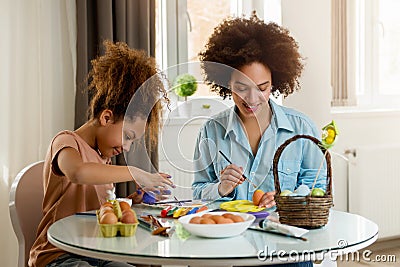 Beautiful African American woman and her daughter coloring Easter eggs Stock Photo