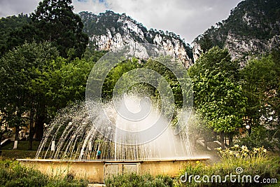 A beautiful artesian fountain, somewhere near the mountains. A beautiful summer day in the park. Many green trees and many plants Stock Photo