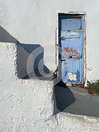 A Beautiful Artful Photograph with a Blue Rustic Door Against a White Washed Building with Steps Stock Photo