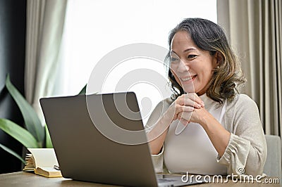 Beautiful Asian-aged businesswoman working in her home living room, using laptop. work from home Stock Photo