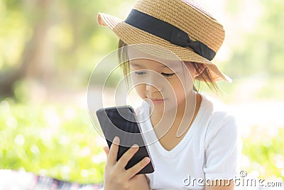 Beautiful asian child smiling using smart mobile phone in the garden, kid have passion playing game digital on smartphone Stock Photo