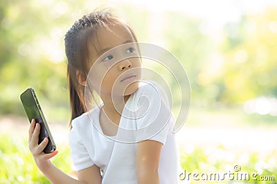 Beautiful asian child smiling using smart mobile phone in the garden, kid have passion playing game digital on smartphone Stock Photo