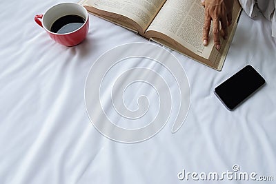 Beautiful asian female sitting on the bed with a cup of coffee and reading a book Stock Photo