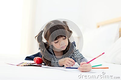 Beautiful Asian girl drawing and doing homework on the bed. Children relax and free time for creative her play. Stock Photo