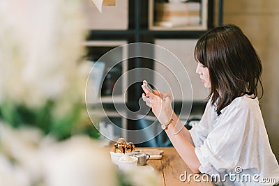 Beautiful Asian girl using smartphone at cafe with chocolate toast and ice cream. Coffee shop dessert and modern casual lifestyle Stock Photo