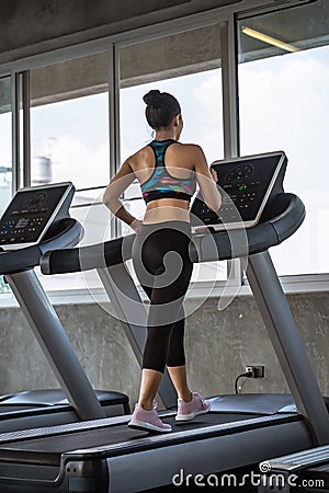 Beautiful asian girl is walking on a treadmill in the gym.She Send your eyes with pleasure in exercise because it makes her Stock Photo