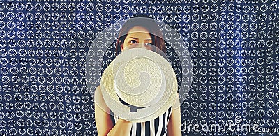Beautiful Asian woman in black and white dress and holding white hat to close in half of her face with blue cotton background Stock Photo