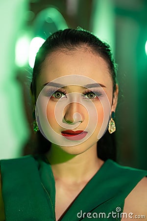 a beautiful Asian woman in a green dress has a very exotic face with ear and body jewelry while Stock Photo