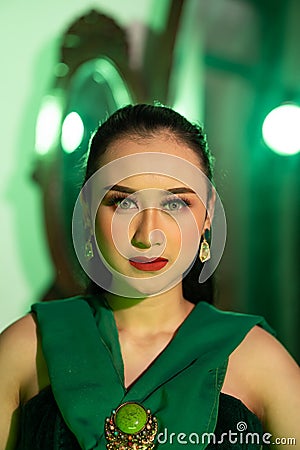 a beautiful Asian woman in a green dress has a very exotic face with ear and body jewelry while Stock Photo