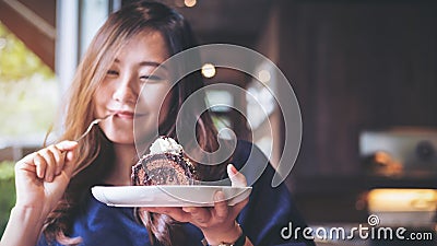 A beautiful Asian woman holding chocolate cake roll and whipped cream and fork with feeling happy and enjoy eating in the cafe Stock Photo