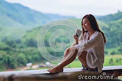 A woman holding and drinking hot coffee on balcony , looking at mountains and green nature Stock Photo