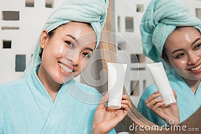 Beautiful asian woman holding tube of facial foam, cream or lotion in front of mirror bathroom Stock Photo