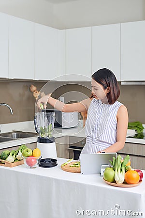 Beautiful Asian Woman juicing making green juice with juice machine in home kitchen. Healthy concept Stock Photo