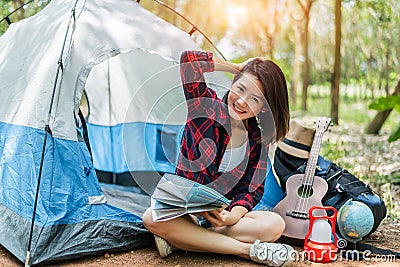 Beautiful Asian woman playing Ukulele in front of camping tent in pine woods. People and Lifestyles concept. Adventure and Travel Stock Photo