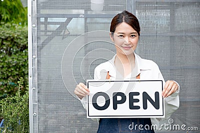 Beautiful Asian woman present banner with word open in front of green house and happy emotion relate with re-open the business Stock Photo