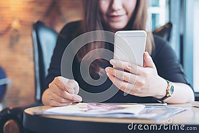 A beautiful Asian woman with smiley face holding and using smart phone with magazines Stock Photo