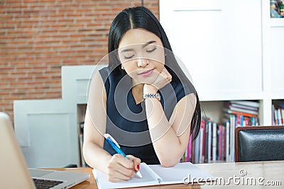 Beautiful Asian woman writing a notebook on table with laptop as Stock Photo