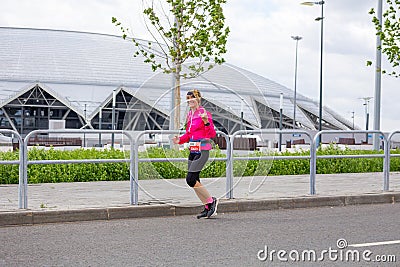 beautiful athletic girl runs at a city sports event, race, against the background of a new stadium Editorial Stock Photo