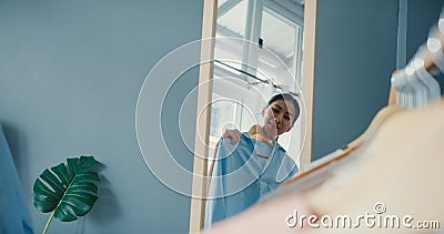 Beautiful attractive Asia lady choosing clothes on clothes rack dressing looking herself in mirror in living room at house. Girl Stock Photo