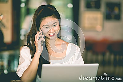 Beautiful Attractive Asian woman working with laptop smile and talking with customer in smartphone to get idea and requirement Stock Photo