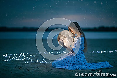 Beautiful attractive girl on a night beach with sand and stars hugs the moon, Artistic Photography Stock Photo