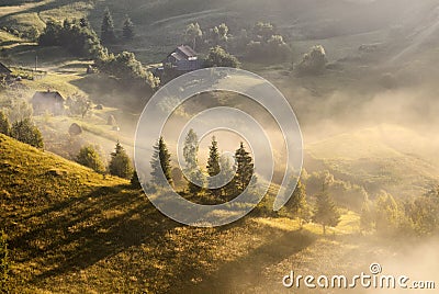 A beautiful autumn foggy landscape with lonely houses and sunny hills. Carpathian rural landscape on sunset in autumn colors. Pic Stock Photo