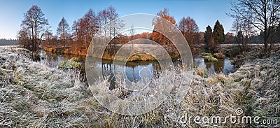 Beautiful autumn morning panorama with frosty grass, small river, falling trees and blue sky. Stock Photo