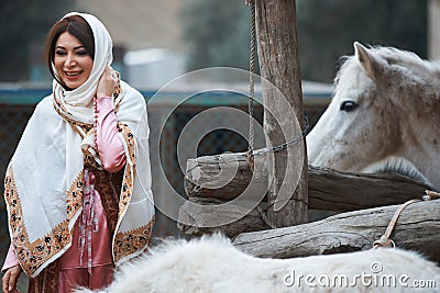 Beautiful azeri woman in traditional Azerbaijani dress standing with white horse Stock Photo