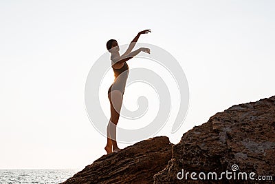 Beautiful ballerina dancing, posing on rock at beach, sea background. Stock Photo